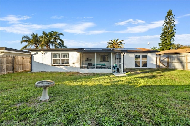 rear view of property with roof mounted solar panels, a lawn, a fenced backyard, and a sunroom