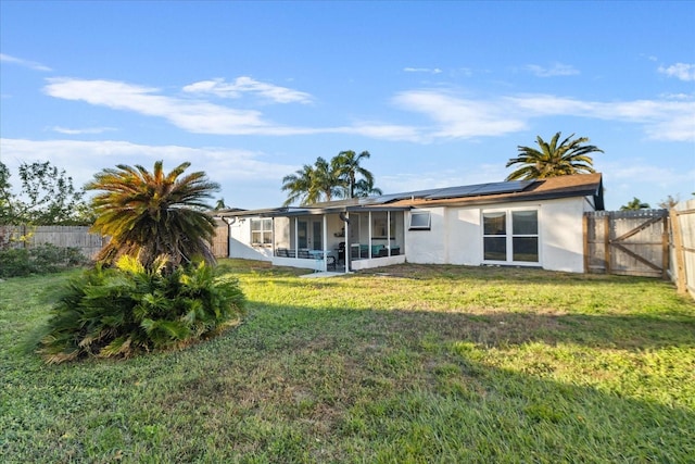 rear view of property featuring a yard, roof mounted solar panels, a fenced backyard, and a sunroom