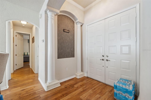entryway with baseboards, decorative columns, arched walkways, crown molding, and light wood-type flooring