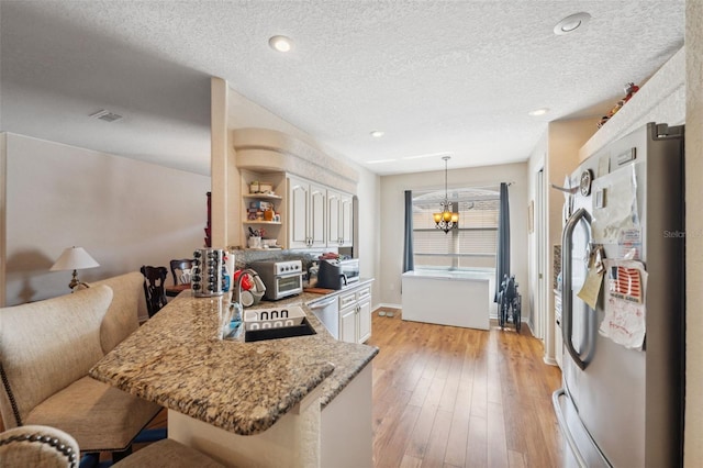 kitchen with visible vents, appliances with stainless steel finishes, a peninsula, light wood-style floors, and a sink