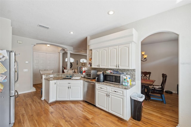 kitchen featuring a peninsula, white cabinets, arched walkways, and appliances with stainless steel finishes
