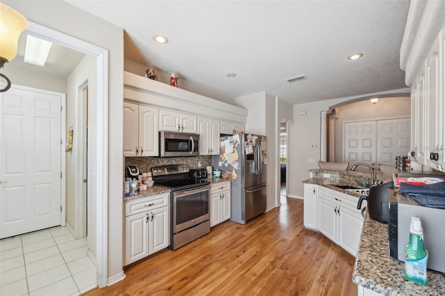 kitchen with a sink, backsplash, white cabinetry, arched walkways, and appliances with stainless steel finishes