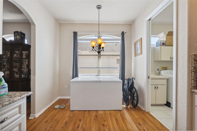 dining space featuring a notable chandelier, light wood-style flooring, washer and clothes dryer, arched walkways, and baseboards