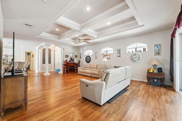 living area with coffered ceiling, arched walkways, light wood finished floors, decorative columns, and ceiling fan