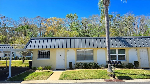 view of front of house with stucco siding, metal roof, a standing seam roof, and a front yard