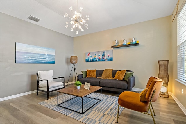 living room featuring a notable chandelier, wood finished floors, visible vents, and baseboards