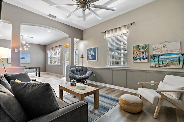 living room with arched walkways, a wainscoted wall, ceiling fan with notable chandelier, and wood finished floors