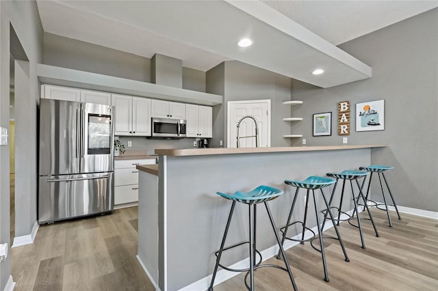 kitchen featuring stainless steel appliances, a peninsula, white cabinets, and light wood finished floors