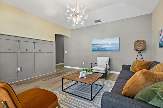 living area with a chandelier, arched walkways, light wood finished floors, baseboards, and visible vents