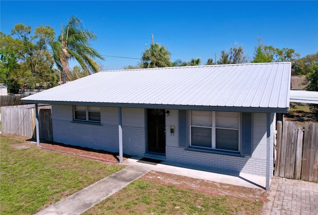 view of front of property with a front lawn, fence, brick siding, and metal roof