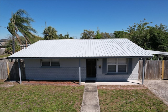 view of front facade with metal roof, brick siding, a front lawn, and fence