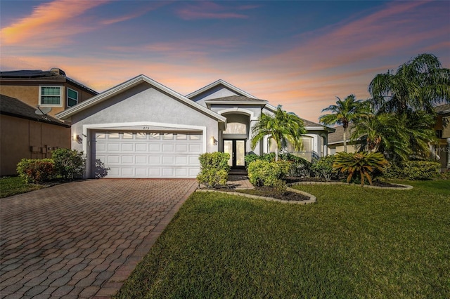 view of front of house featuring a front yard, decorative driveway, a garage, and stucco siding