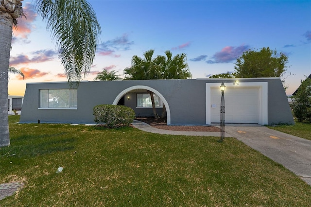 view of front of home featuring stucco siding, a lawn, a garage, and driveway