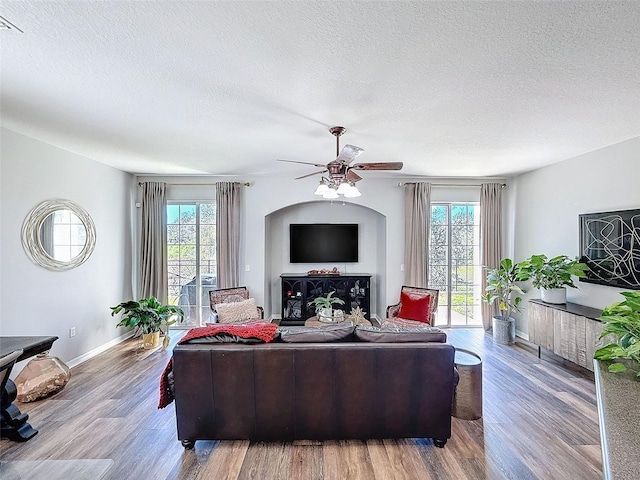 living area with ceiling fan, a textured ceiling, wood finished floors, and a healthy amount of sunlight