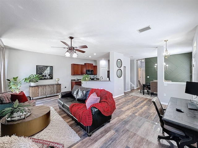 living room with ceiling fan with notable chandelier, wood finished floors, visible vents, and baseboards