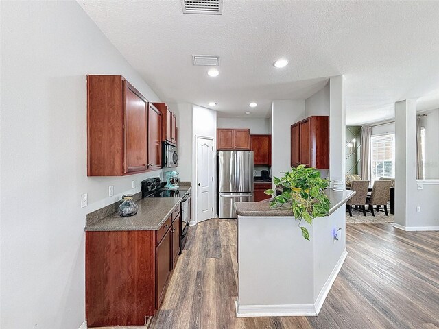 kitchen featuring visible vents, black appliances, a textured ceiling, wood finished floors, and a peninsula