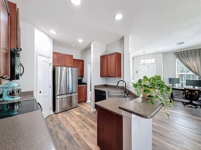 kitchen with a peninsula, freestanding refrigerator, a sink, dishwasher, and light wood-type flooring