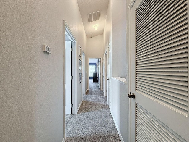 hallway featuring a textured wall, visible vents, baseboards, and carpet floors