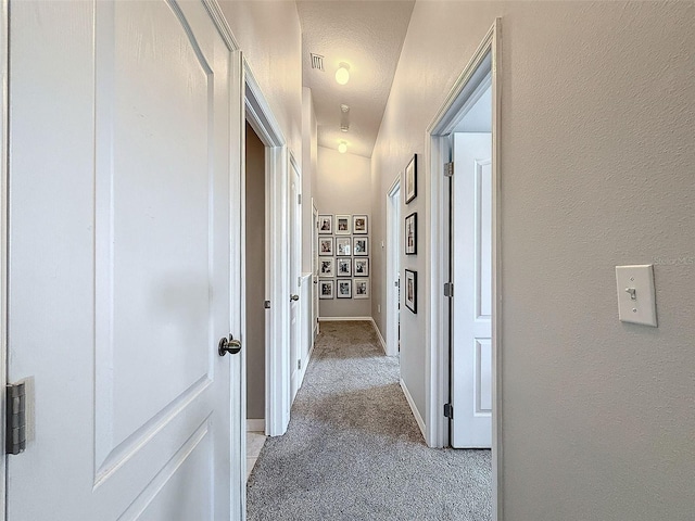 hallway with visible vents, light carpet, a textured ceiling, baseboards, and a textured wall