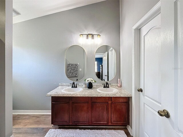 bathroom with double vanity, wood finished floors, baseboards, and a sink