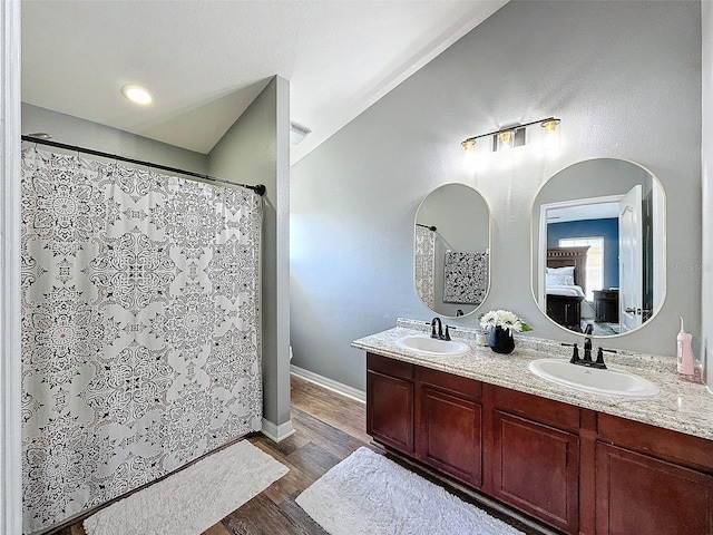 bathroom with double vanity, connected bathroom, wood finished floors, and a sink