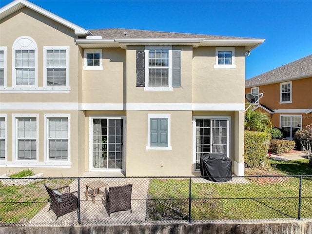 back of house featuring stucco siding, a lawn, fence private yard, and a shingled roof