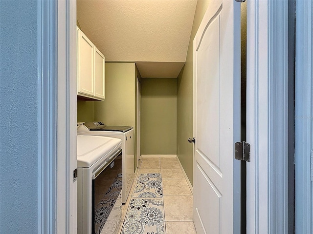 clothes washing area featuring baseboards, washing machine and dryer, light tile patterned flooring, cabinet space, and a textured ceiling