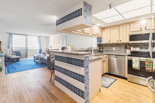 kitchen with light wood-type flooring, a sink, open floor plan, appliances with stainless steel finishes, and decorative backsplash