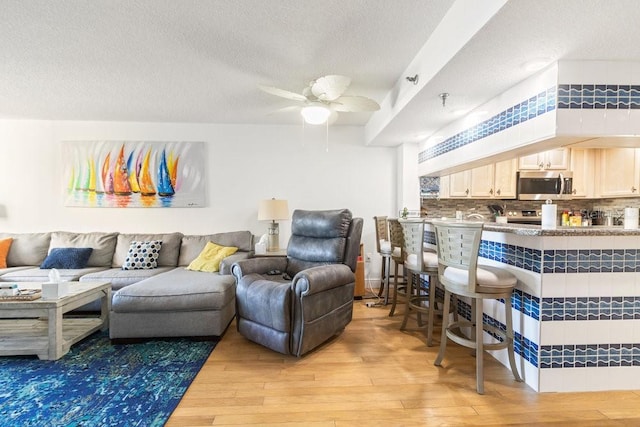 living area featuring light wood-style flooring, a textured ceiling, and ceiling fan