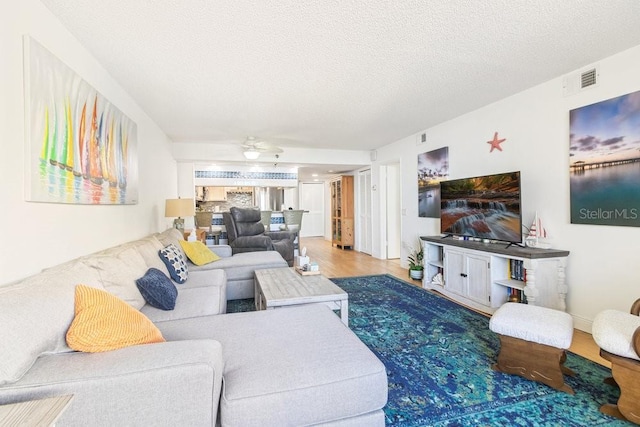 living room featuring a textured ceiling, wood finished floors, visible vents, and ceiling fan