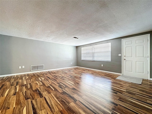 unfurnished living room featuring a textured ceiling, wood finished floors, visible vents, and baseboards