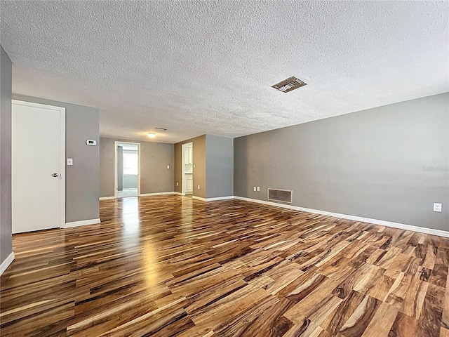 unfurnished room featuring a textured ceiling, wood finished floors, visible vents, and baseboards