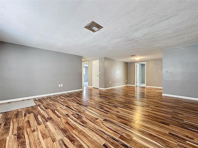 empty room featuring visible vents, wood finished floors, baseboards, and a textured ceiling