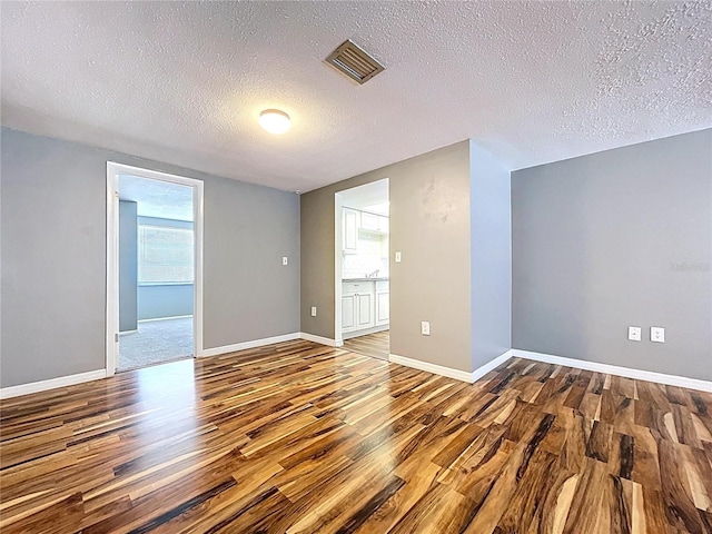 spare room with a textured ceiling, wood finished floors, visible vents, and baseboards