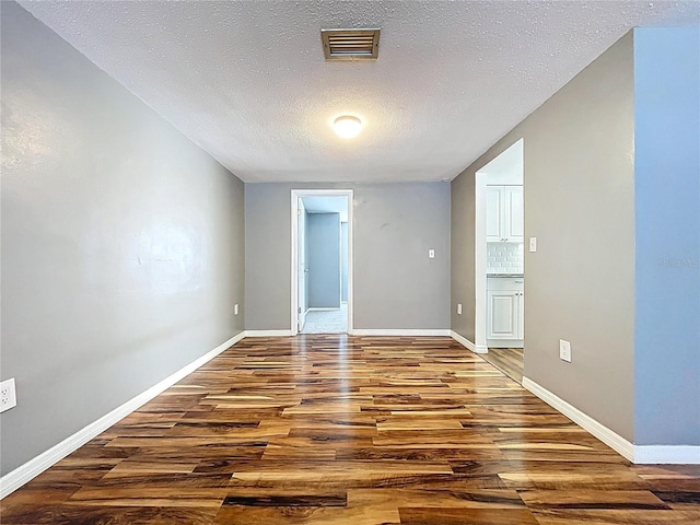 spare room with a textured ceiling, wood finished floors, visible vents, and baseboards