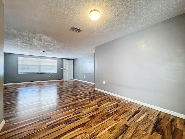 empty room with visible vents, baseboards, a textured ceiling, and dark wood-style floors