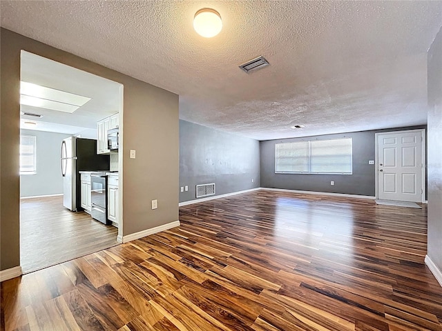 unfurnished living room with a wealth of natural light, visible vents, and dark wood-type flooring