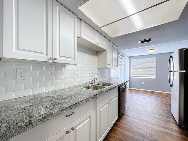 kitchen with a sink, black dishwasher, decorative backsplash, freestanding refrigerator, and dark wood-style flooring