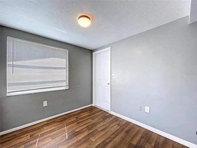 unfurnished room featuring baseboards, dark wood-type flooring, and a textured ceiling