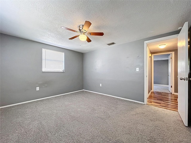 carpeted spare room featuring baseboards, a ceiling fan, visible vents, and a textured ceiling