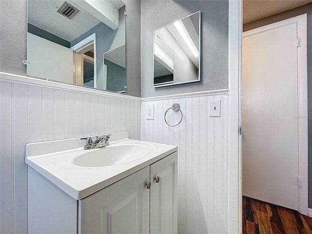 bathroom with visible vents, wainscoting, a textured ceiling, and wood finished floors