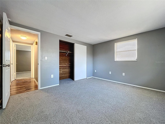 unfurnished bedroom featuring visible vents, carpet floors, a textured ceiling, and a closet