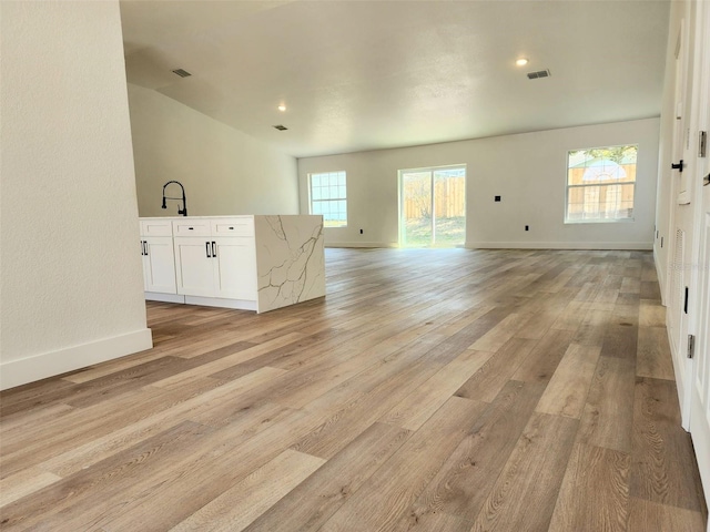 unfurnished living room featuring visible vents, light wood-style flooring, baseboards, and a sink