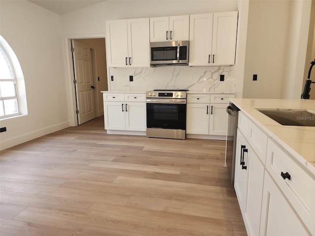 1032 Concert Ave, Spring Hill, FL 34609 - kitchen featuring a sink, backsplash, stainless steel appliances, light wood-style floors, and white cabinets