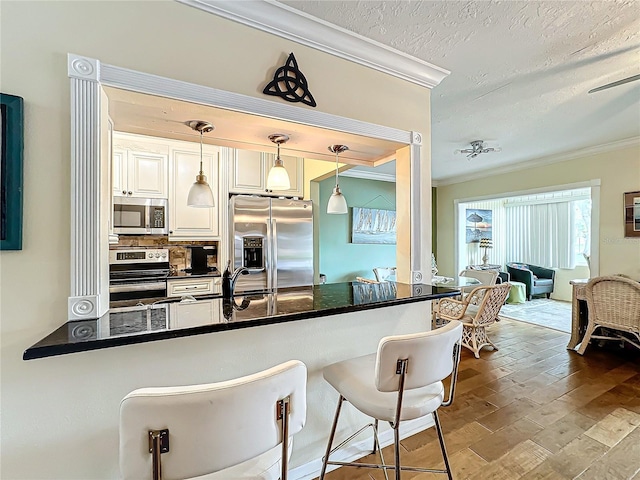 kitchen with a breakfast bar, ornamental molding, stainless steel appliances, a textured ceiling, and tasteful backsplash