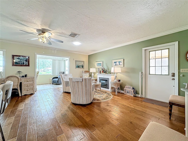 living area with visible vents, ornamental molding, hardwood / wood-style floors, a glass covered fireplace, and a ceiling fan