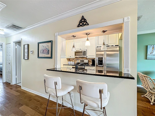 kitchen with visible vents, dark wood finished floors, ornamental molding, stainless steel appliances, and dark countertops