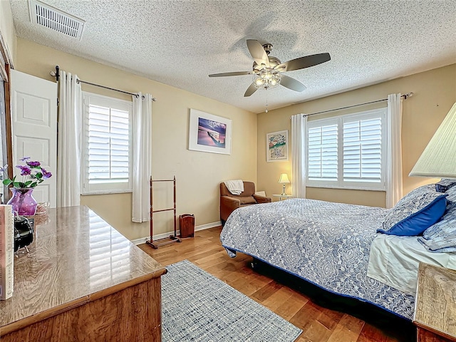 bedroom featuring visible vents, a textured ceiling, light wood-type flooring, and ceiling fan