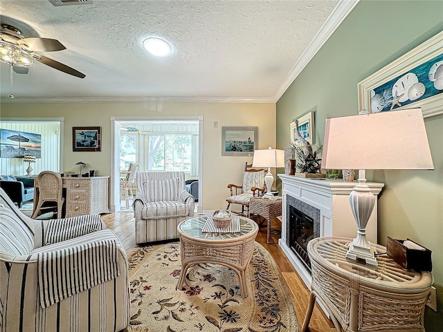 living room featuring a ceiling fan, light wood-style flooring, crown molding, and a textured ceiling