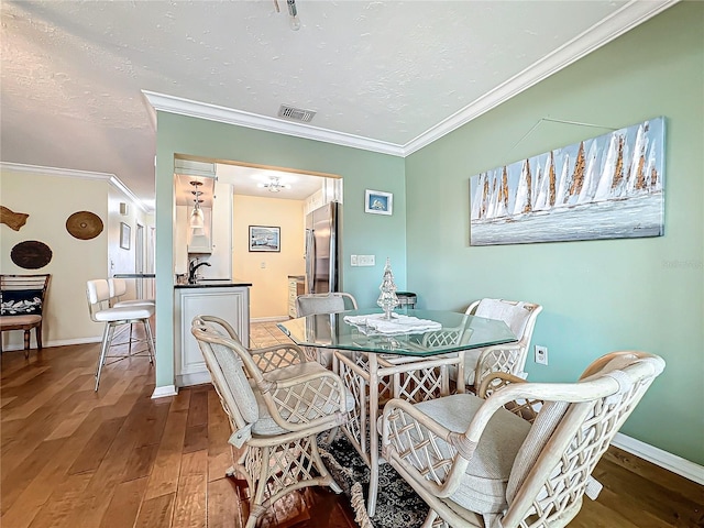 dining space with baseboards, a textured ceiling, wood finished floors, and ornamental molding